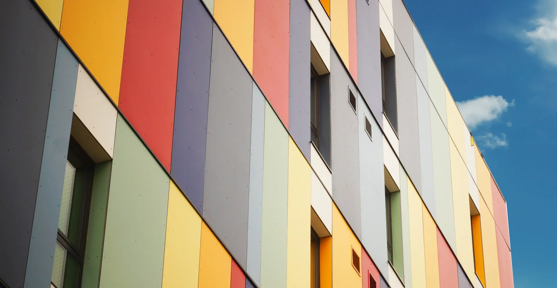 A building facade with vertical panels in vibrant colors like red, yellow, blue, and green against a clear blue sky, conveying a lively and modern feel.