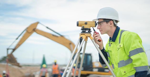 Male engineer working with survey equipment on construction site and worker background