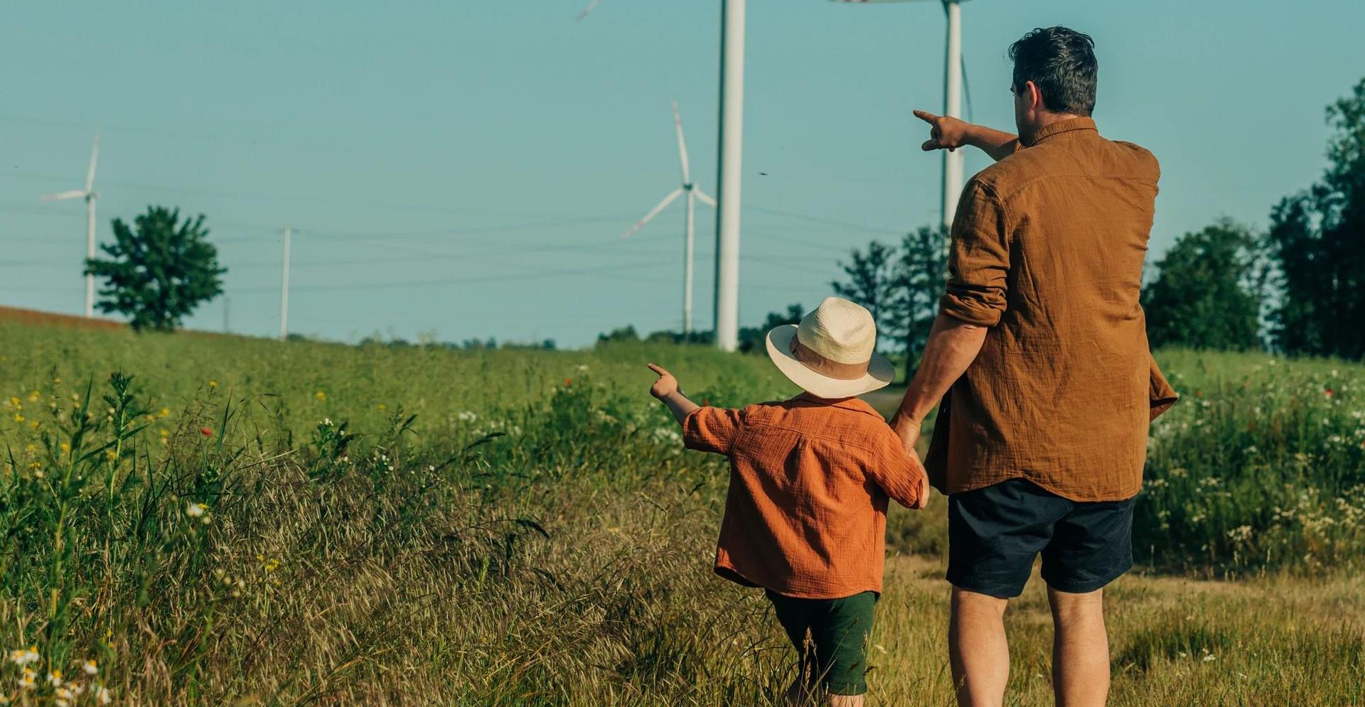 Father and son gesturing towards wind turbines at field