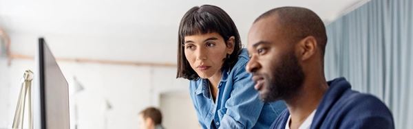 Two businesspeople looking at desktop computer monitor and discussing work at desk