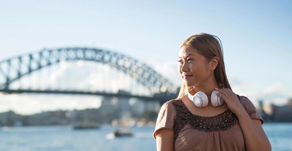 Woman in Sydney wearing headphones with Sydney Harbour Bridge in the background.
