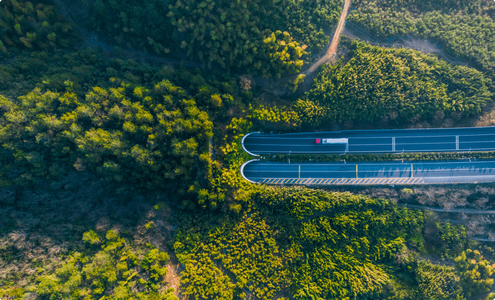 Vue aérienne d'une autoroute sinueuse entourée d'une forêt verdoyante, mettant en valeur la beauté naturelle du paysage.