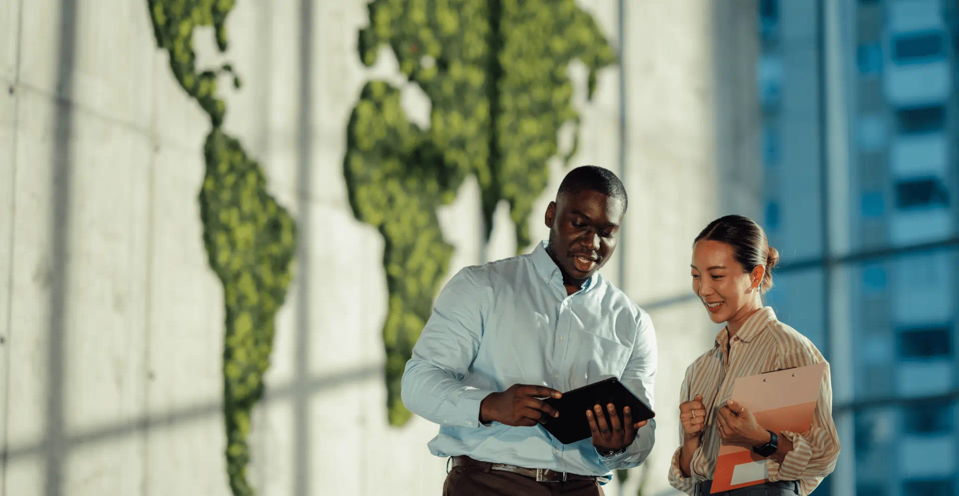 Two business people stand in front of a large world map and discuss global strategies and opportunities.