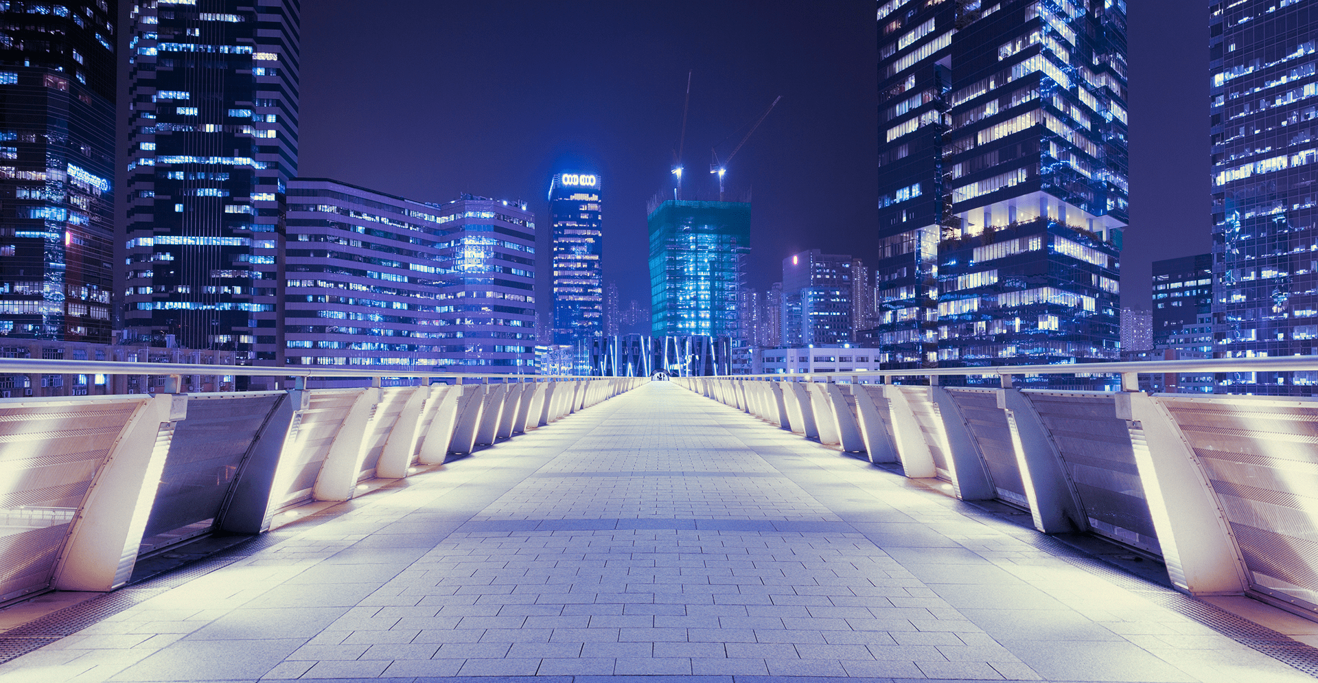 A peaceful walkway in front of a city skyline at night, with soft lights casting a warm glow on the path.