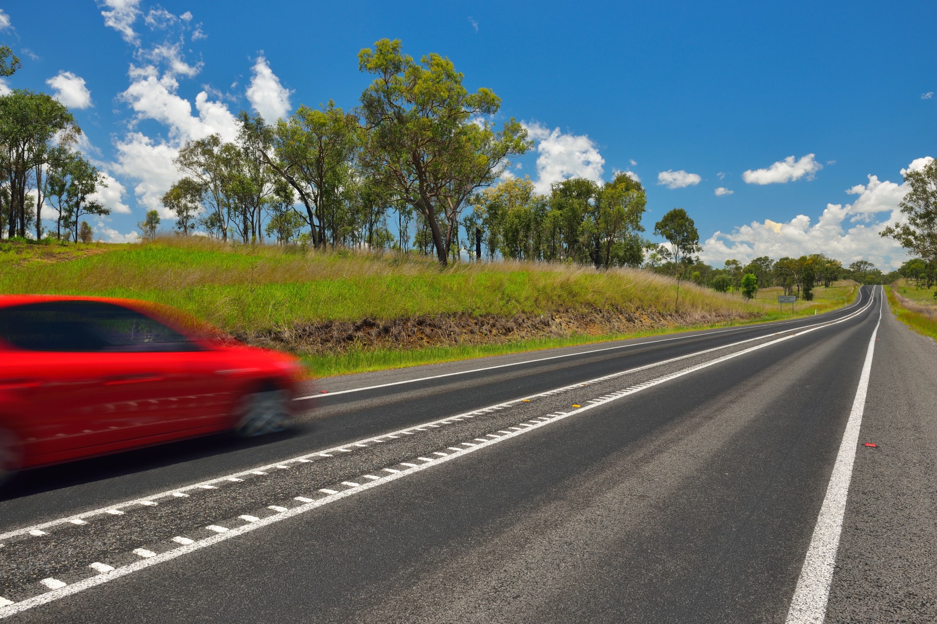 Image of a red car driving across a countryside road.