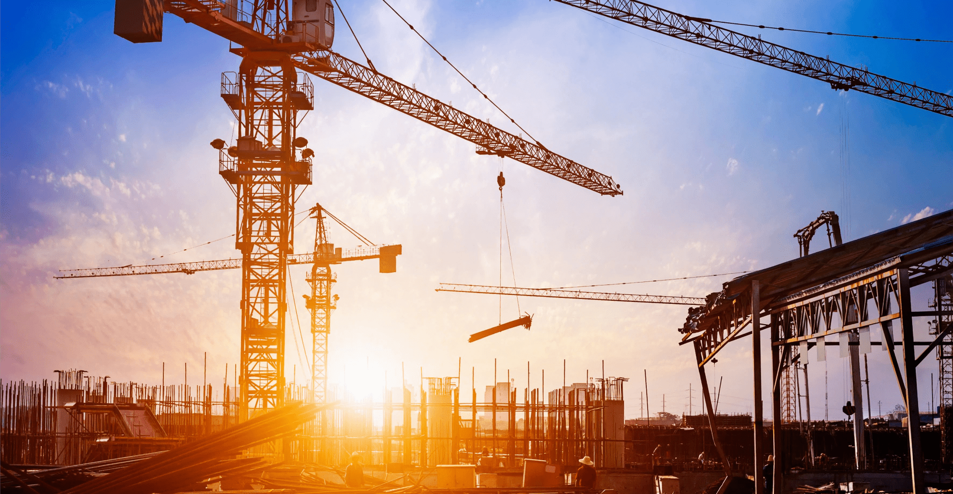 Silhouetted construction cranes against a vibrant sunset.