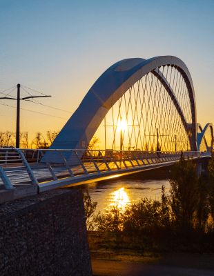 Pont en arc au-dessus de l'eau avec voie de tramway et coucher de soleil en arrière-plan.