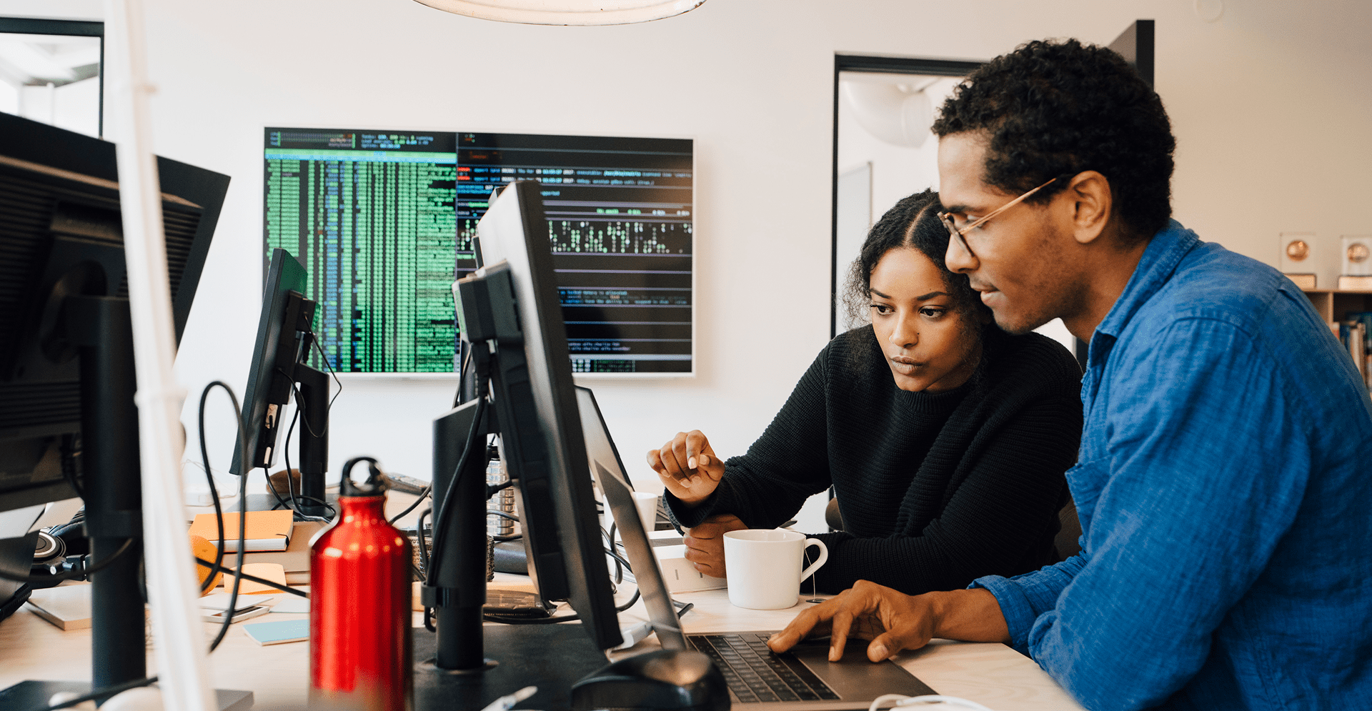 Two individuals engaged in computer work at desks in a contemporary office environment.