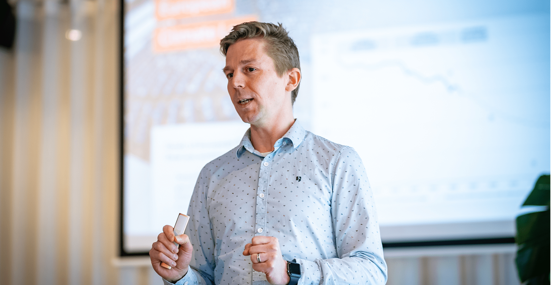 A man presenting at a conference, standing at a podium with a projector screen behind him displaying slides.