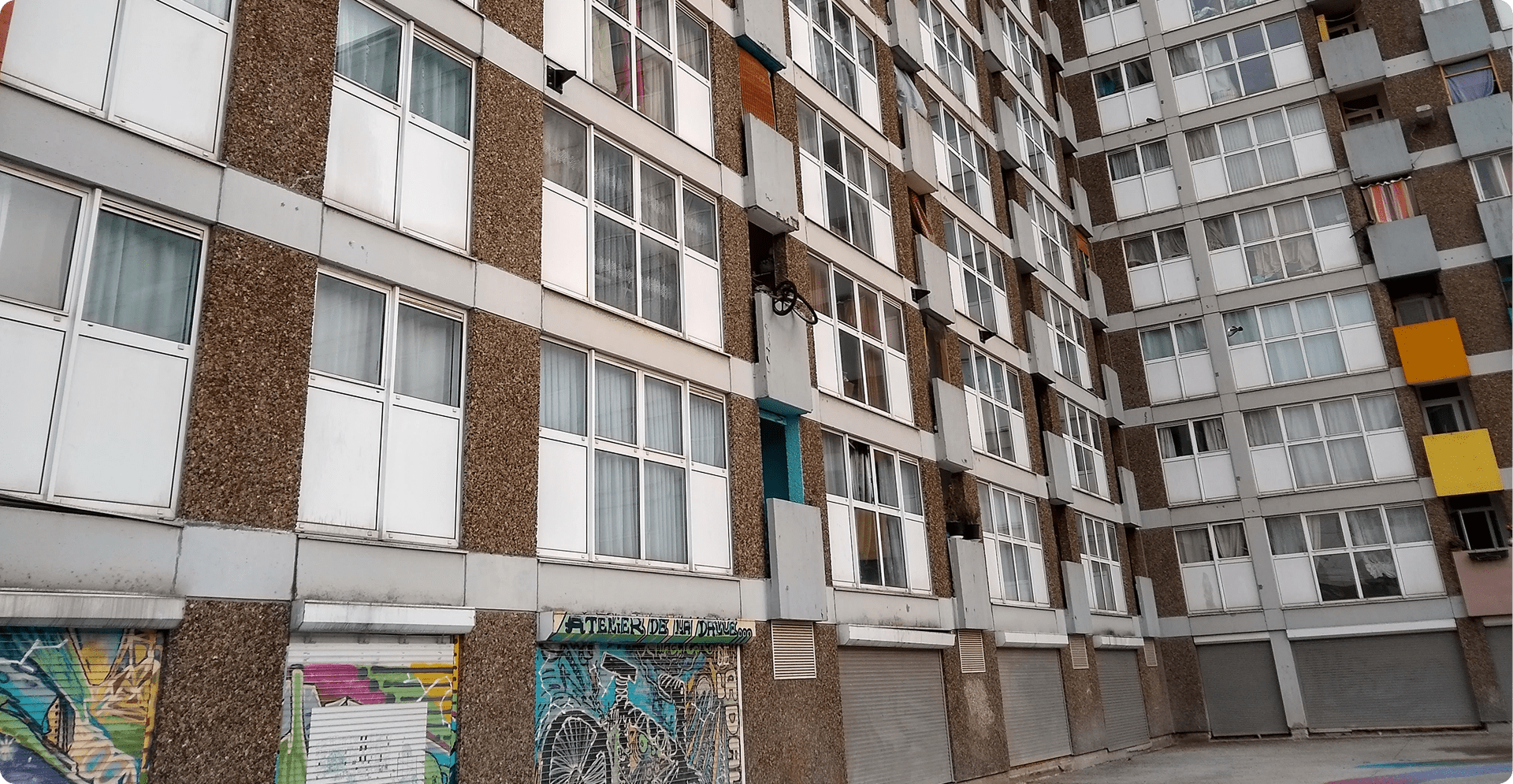 Urban apartment building facade with rows of windows, colorful balcony panels, and ground-floor graffiti storefronts.