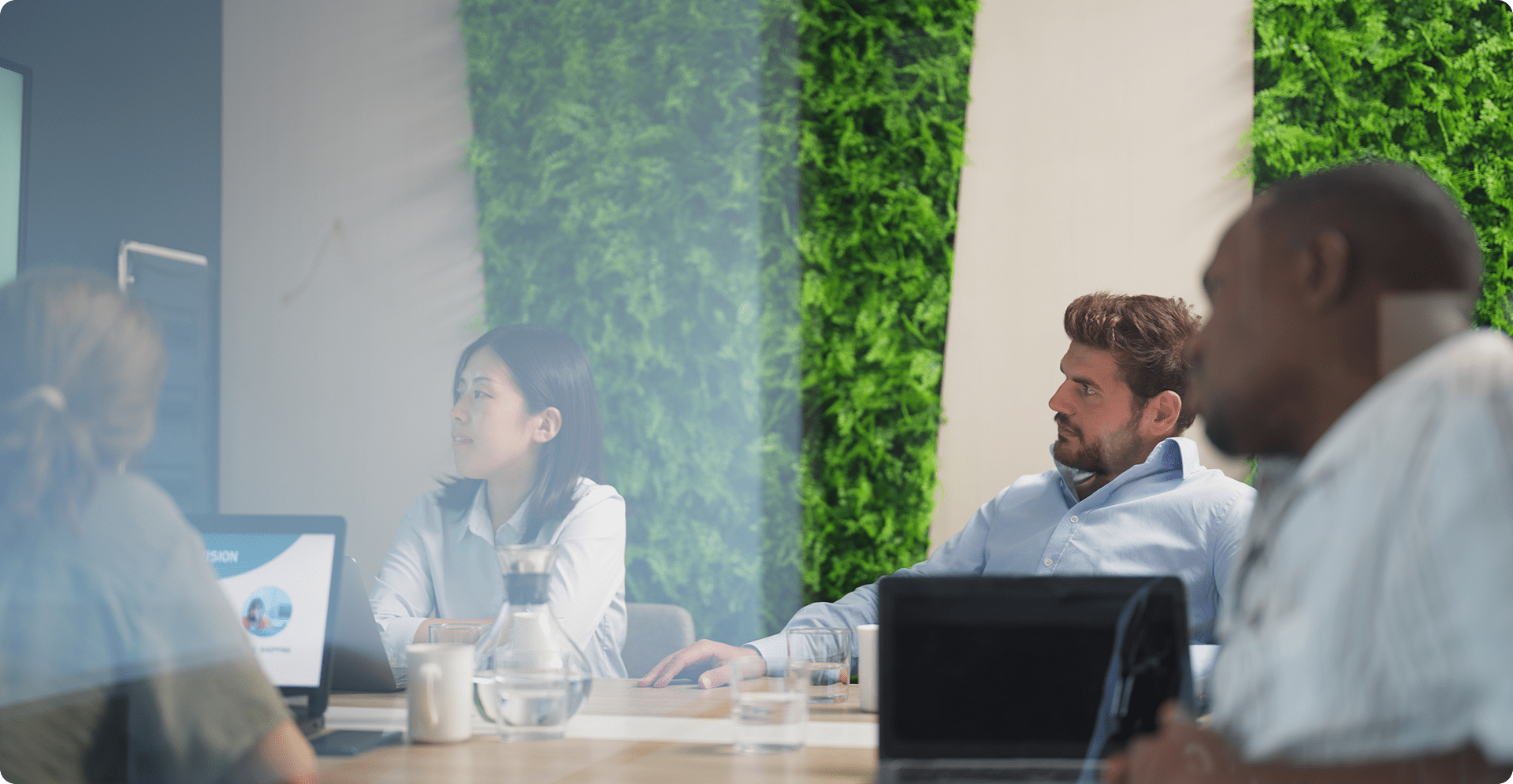 Modern office meeting with people collaborating in front of a green plant wall.