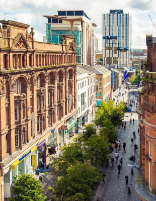 A bustling city street filled with people walking among tall buildings under a clear sky.