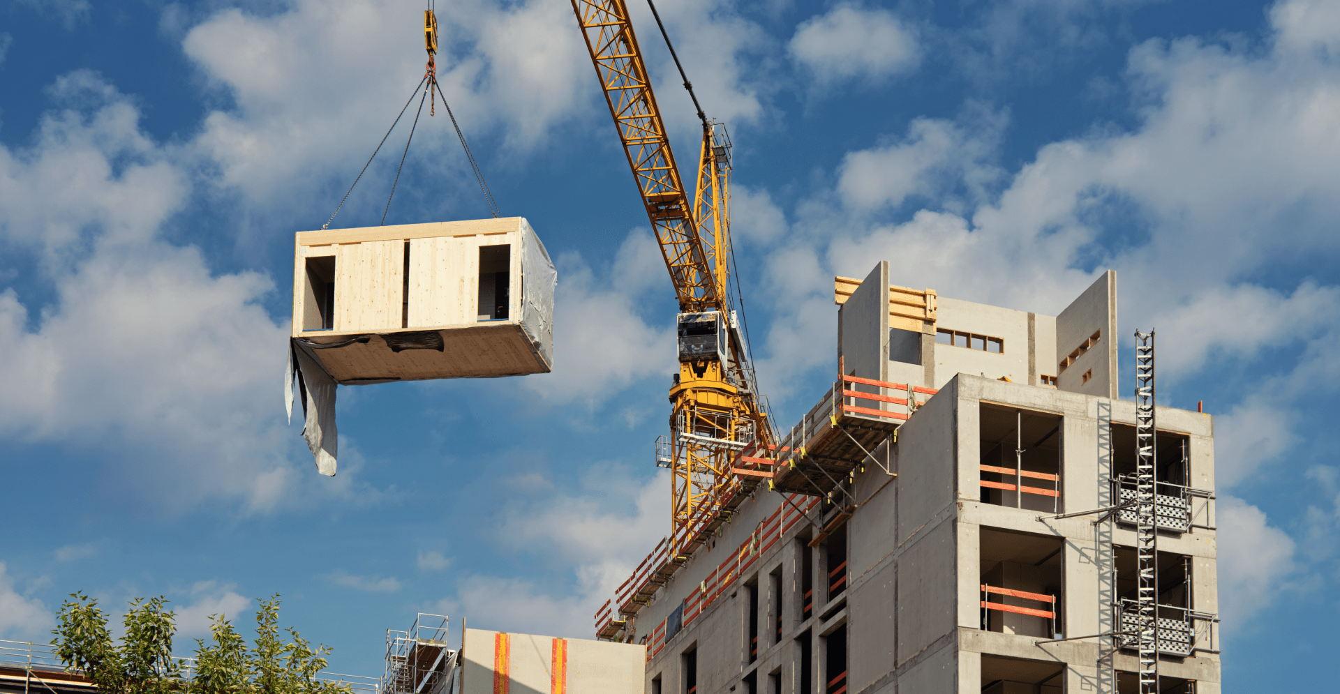 Een gele kraan heist bouwmaterialen op een werf van een woningbouw.