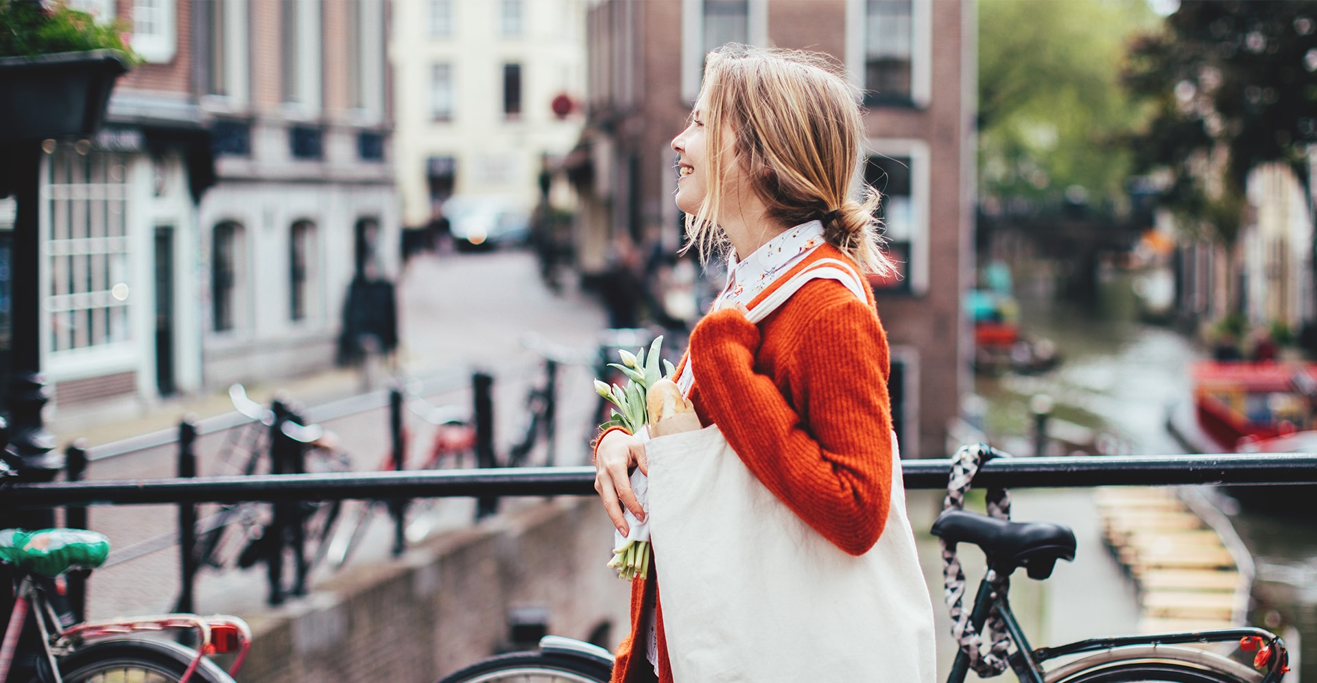 Vrouw met tas over schouder en bos tulpen lopend over brug van Amsterdamse grachten 