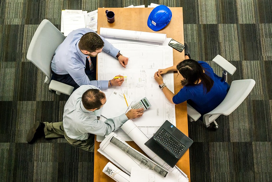 Wat doet een omgevingsmanager nou eigenlijk Drie mensen overleggen het ontwerp zittend aan een tafel.