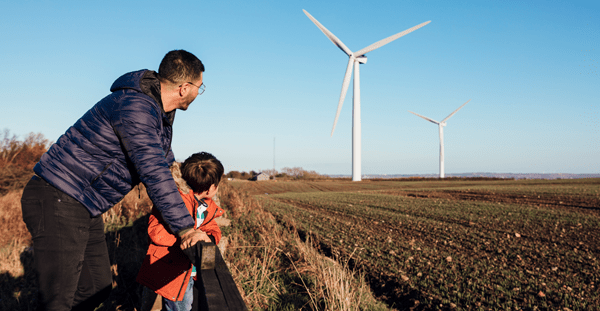 A man and child stand in front of wind turbines, symbolizing renewable energy and a sustainable future.