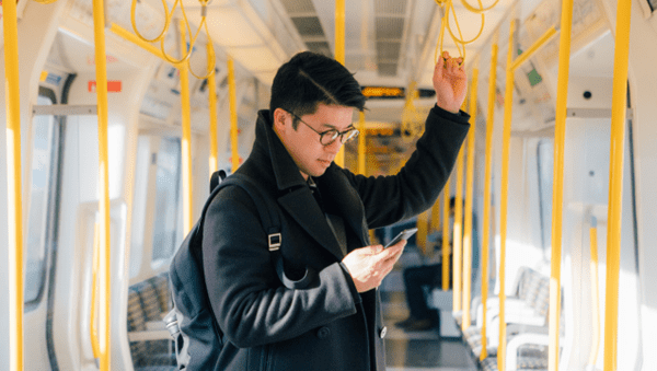 A man standing on a train, engrossed in his phone.
