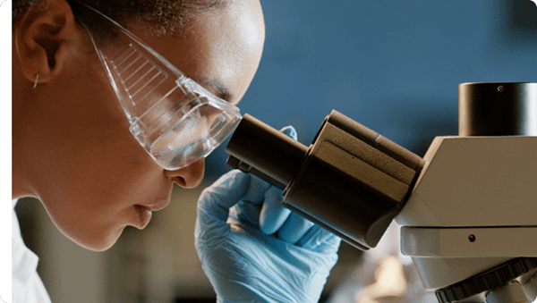 Female scientist in lab coat examining specimen under microscope.