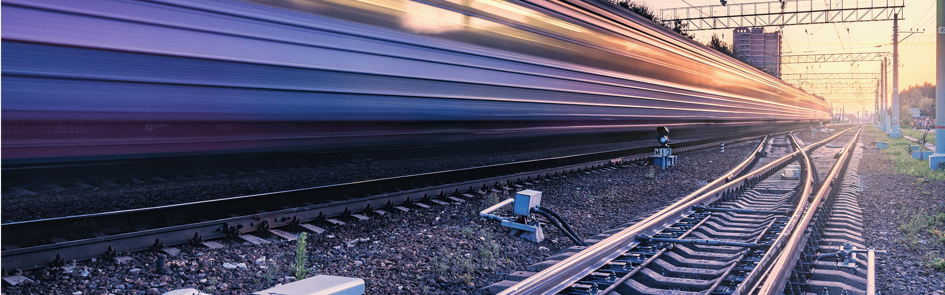 A train journeys down the tracks, framed by a stunning sunset that casts a golden glow over the landscape.