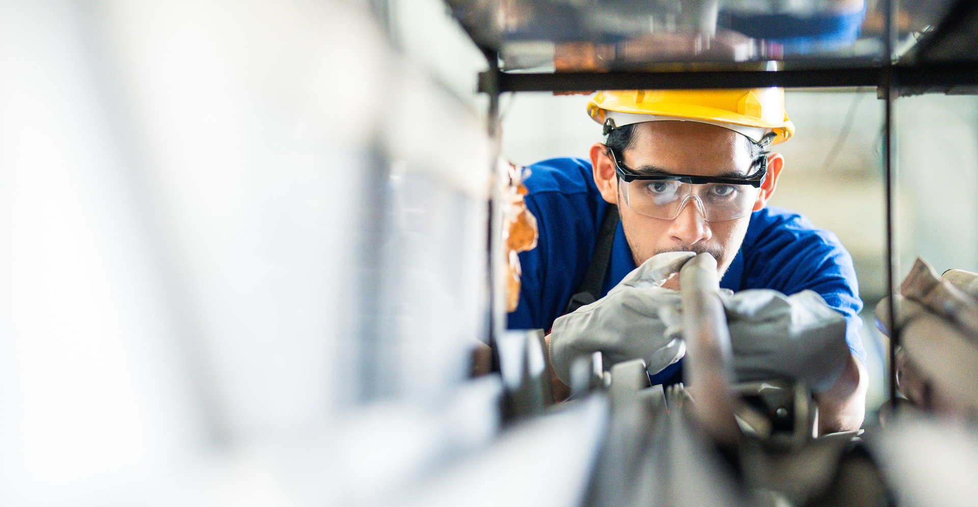 A worker in a blue shirt and hard hat is engaged in operating a machine, demonstrating skill and concentration.