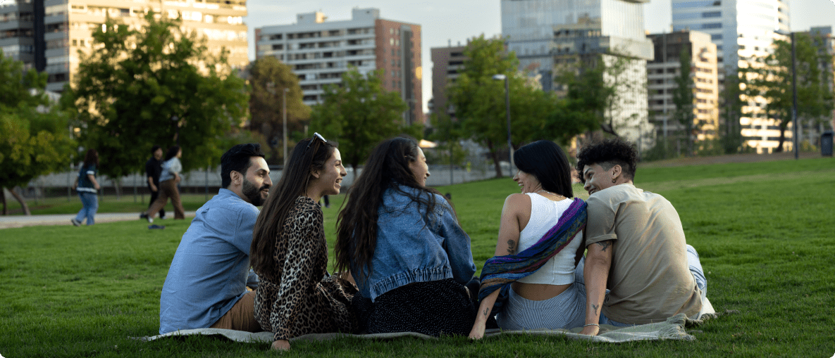 Friends gathered on the grass in a park, sharing smiles and conversation on a bright, sunny day.