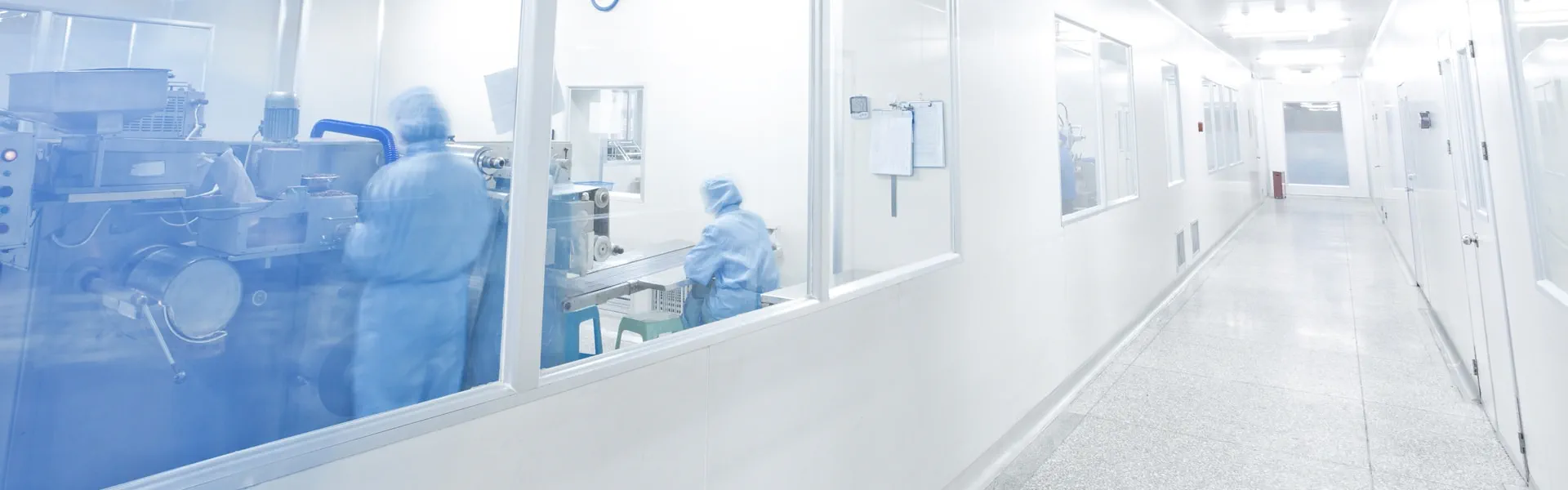 A lengthy corridor with glass panels and a room occupied by individuals wearing blue suits.