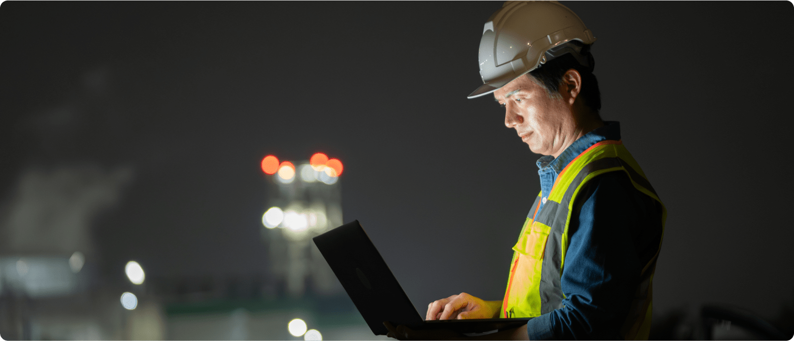A man in a hard hat and safety vest engages with a laptop, highlighting the integration of safety and digital tools in construction.