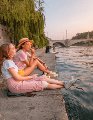 Three girls sitting on the riverbank, enjoying the view and the tranquility of the flowing water.