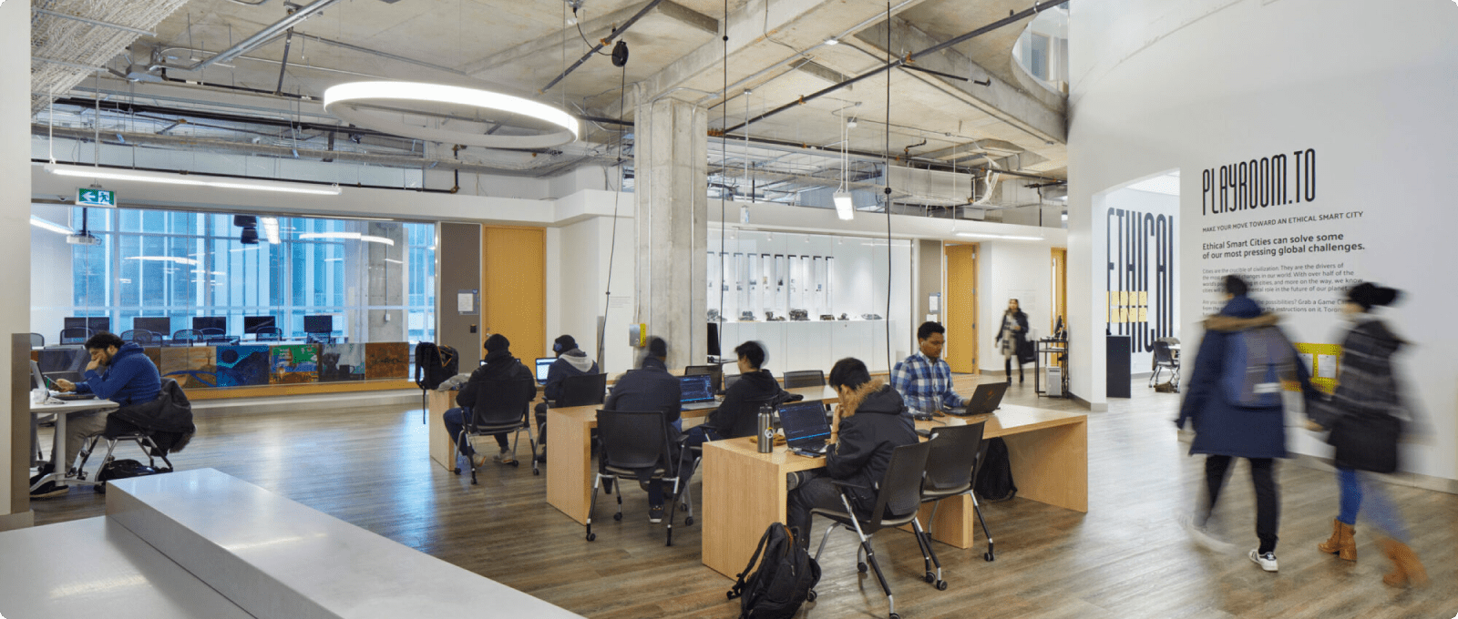 A group of individuals seated at desks in a modern office environment, engaged in various work activities.