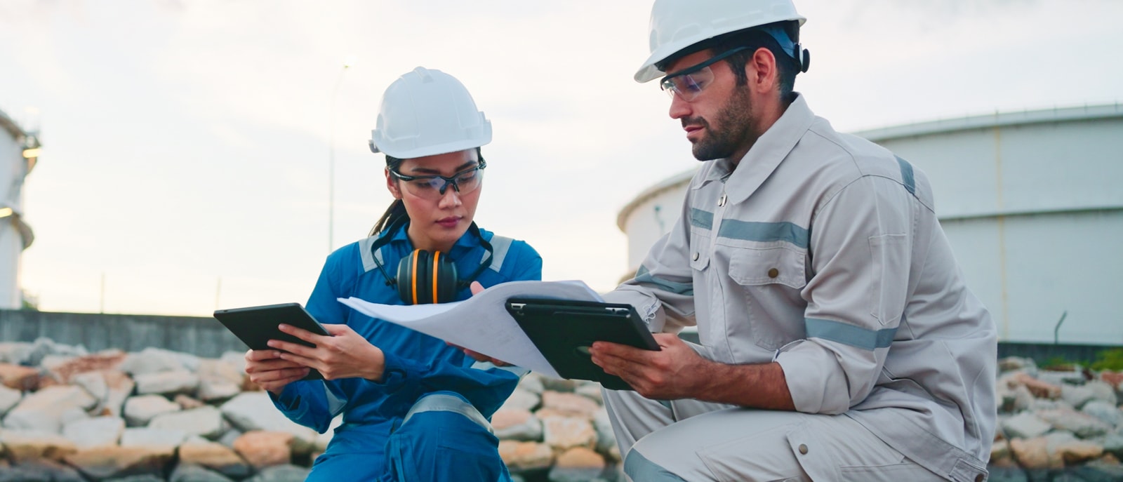 Two people in hard hats discussing plans or data at a construction site.