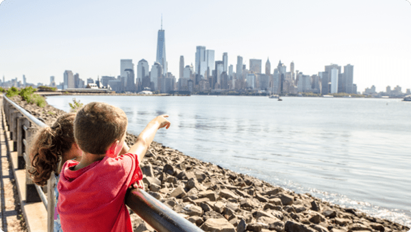 Two children gazing at the water with the city skyline in the background, captivated by the scenic view.