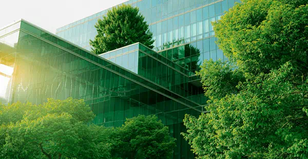 Green glass building blending with nature, surrounded by trees.