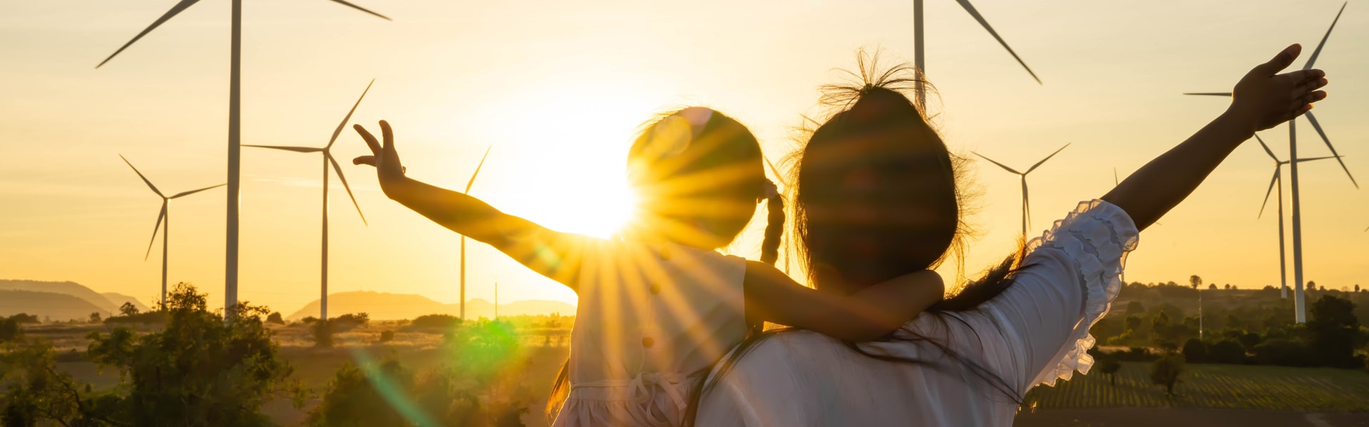 Two individuals stand before wind turbines, silhouetted against a vibrant sunset sky, capturing a moment of renewable energy.