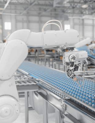A robotic arm carefully handling vials on a conveyor belt inside a manufacturing factory.