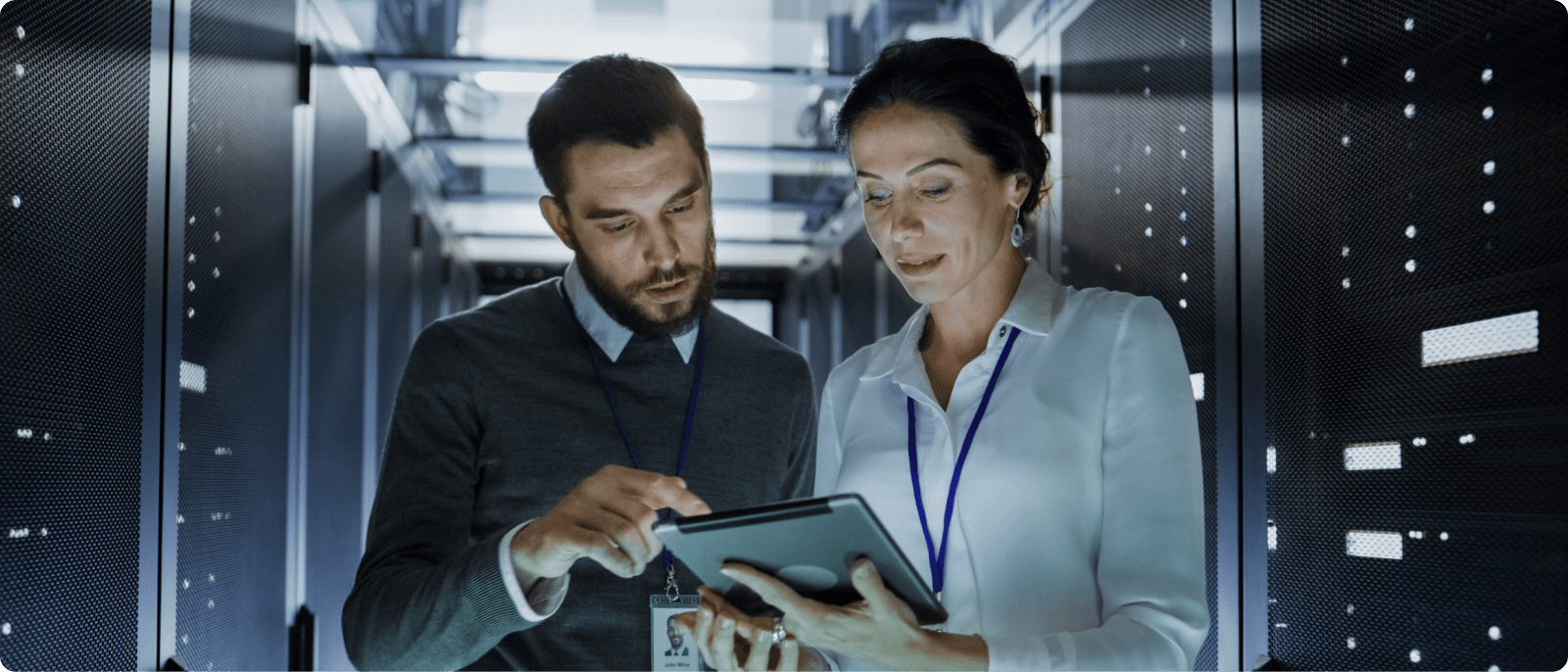 Two individuals examining a tablet while surrounded by server racks in a data center.