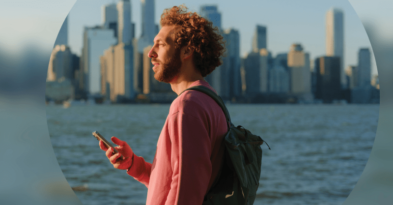 A man with a backpack stands by a tranquil body of water, gazing at the serene landscape before him.