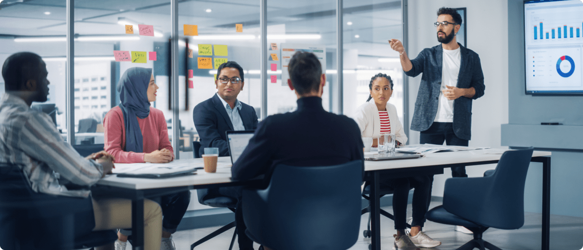 A group of diverse individuals seated around a conference table in a modern office setting, engaged in discussion.