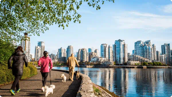 People walking dogs on a waterside trail with downtown skyline in the distance.