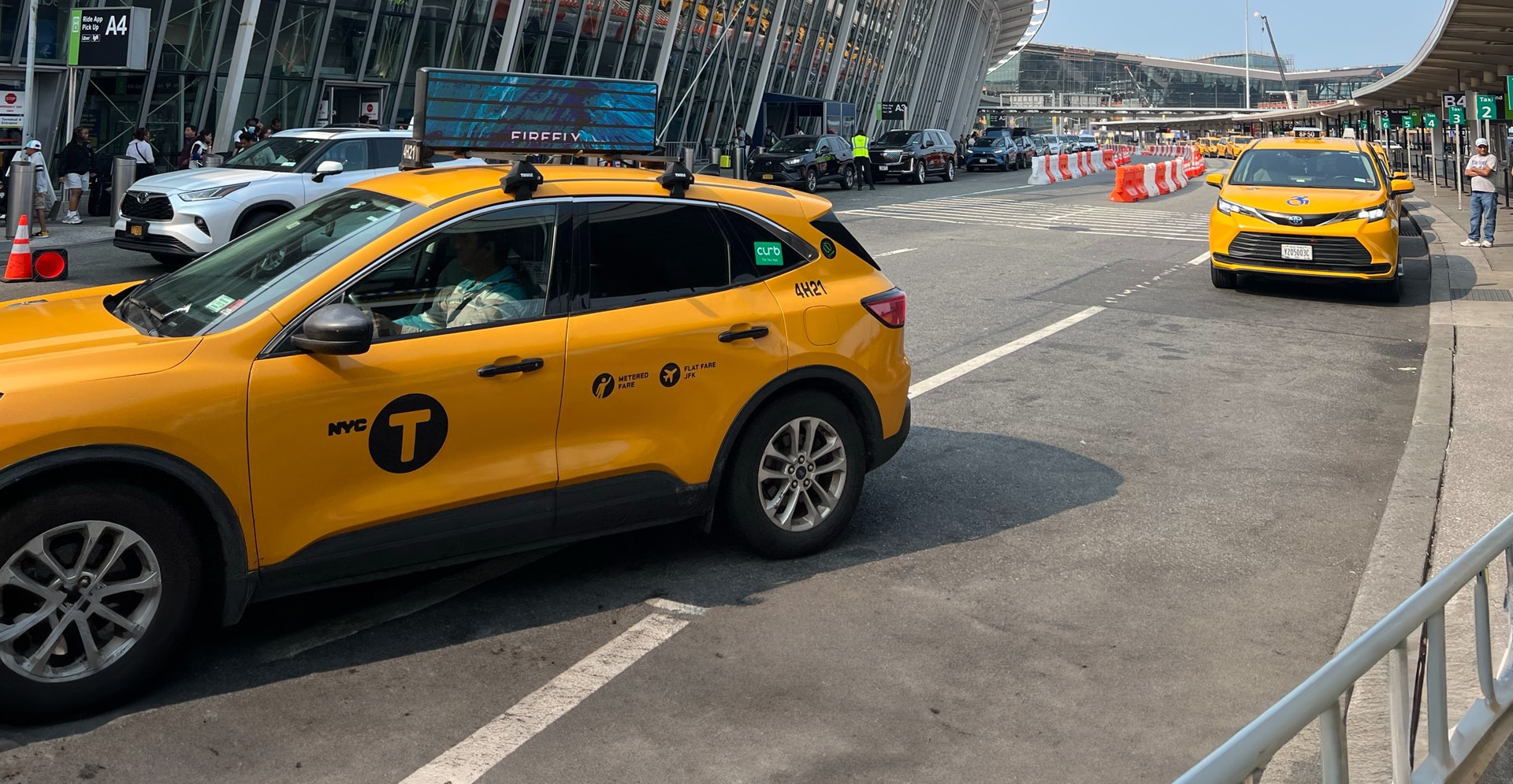 A yellow taxi cab navigates an airport as pedestrians walk by, capturing the vibrant urban atmosphere.