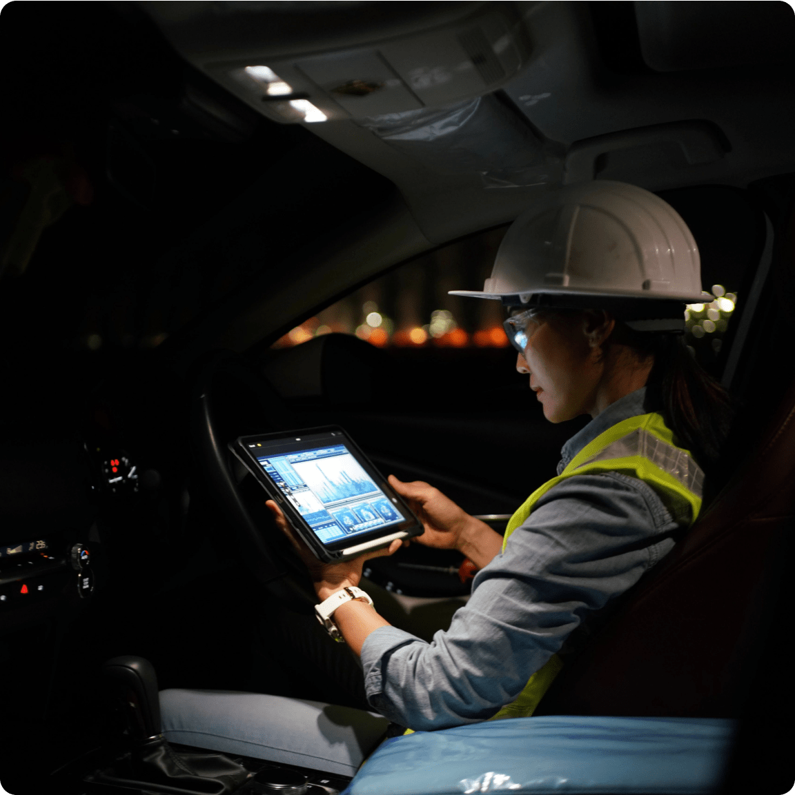 A woman in a hard hat and safety vest is engaged with a tablet computer, demonstrating safety and technology in construction.