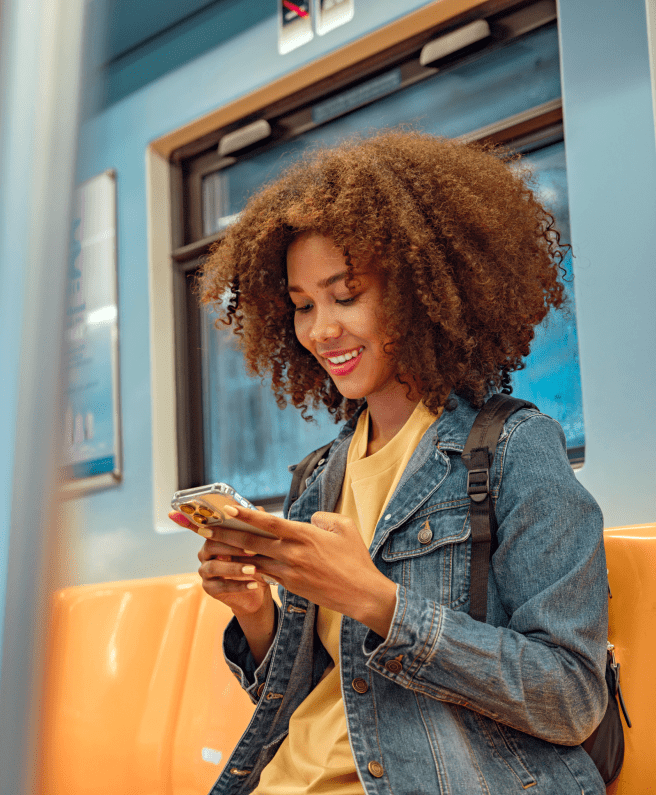 A woman with curly hair sitting on a train, looking at her phone with a thoughtful expression.