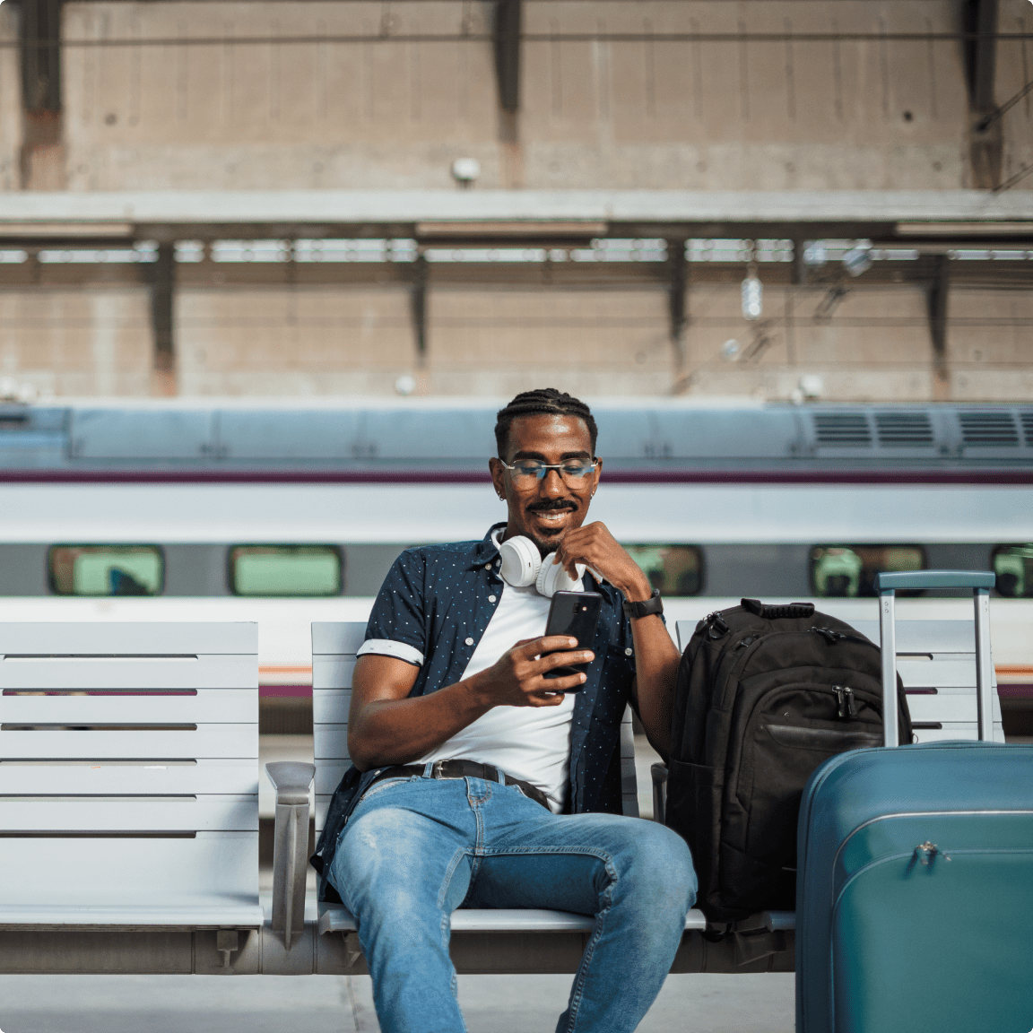 A man seated on a bench, surrounded by his luggage, while using his cell phone.