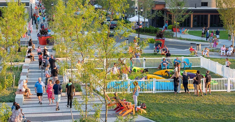 People walking down a sidewalk next to a park.