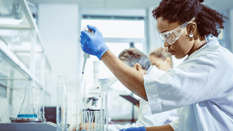 A woman wearing a lab coat is engaged in scientific work, analyzing a test tube in a well-equipped laboratory environment.