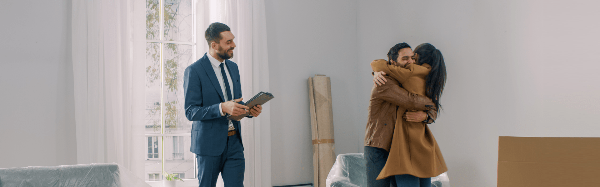 A living room scene featuring a couple hugging amidst boxes and furniture.