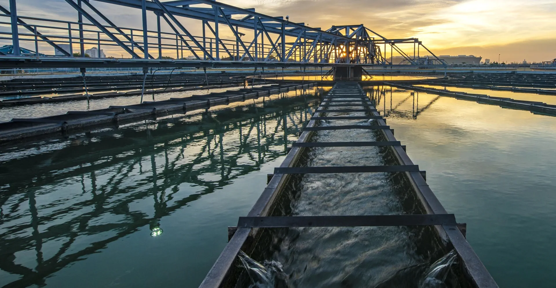 Sunset view of a water treatment plant, featuring large tanks and pipes.