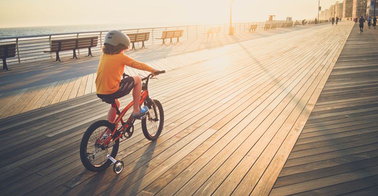 A child riding a bike on a boardwalk, surrounded by a scenic view of the ocean.