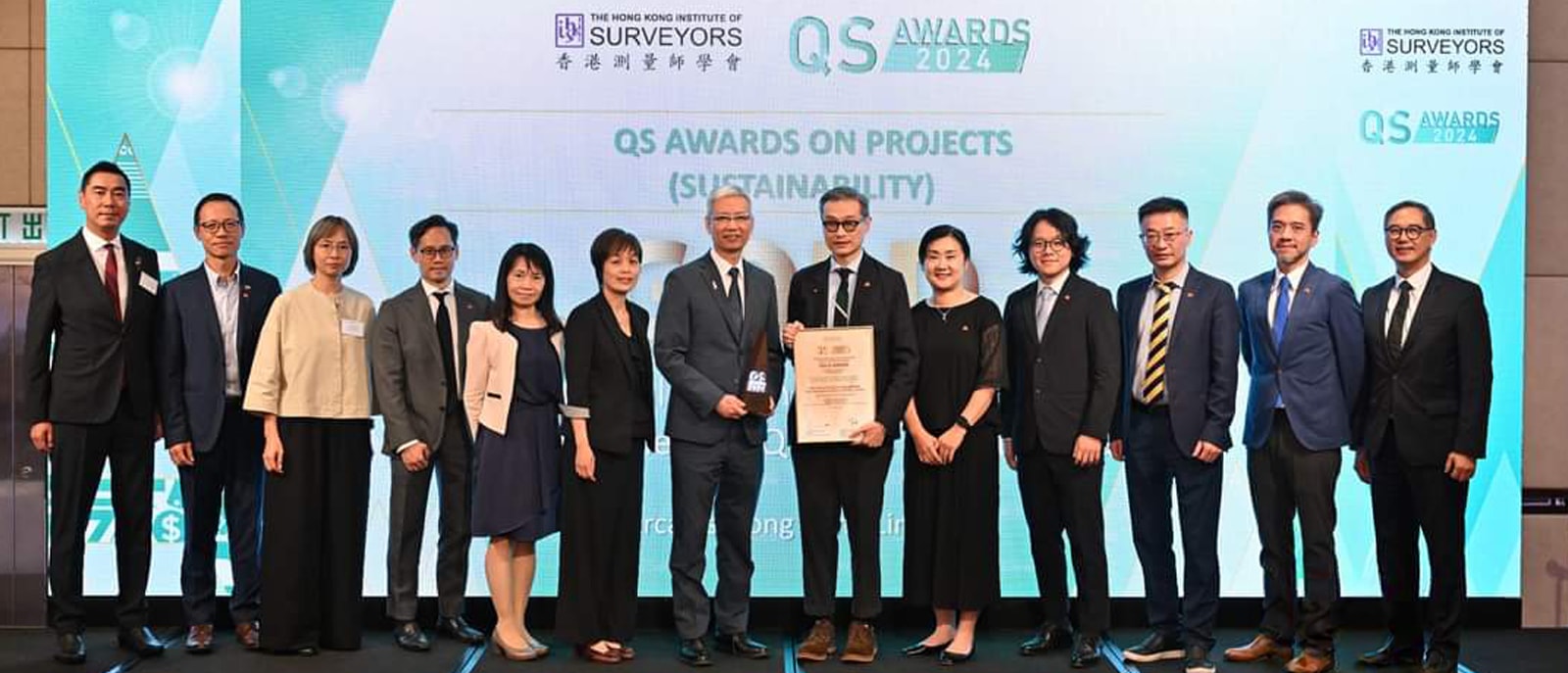 A diverse group of individuals in formal attire standing on stage, taking a picture with award on stage.