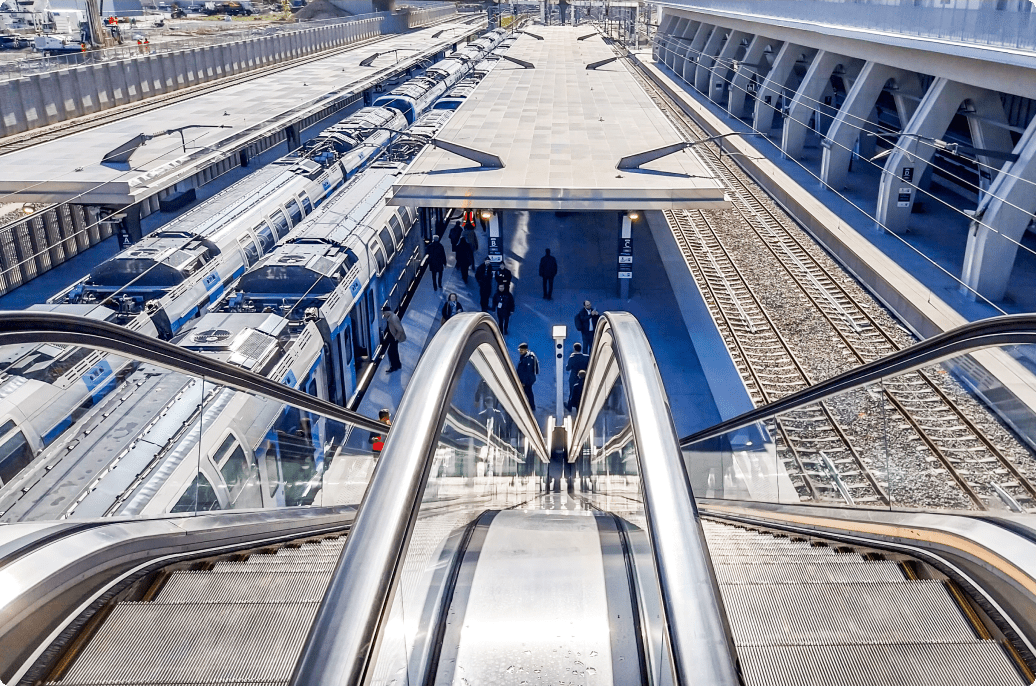 An escalator at a train station, flanked by two trains, illustrating the bustling transit environment. 