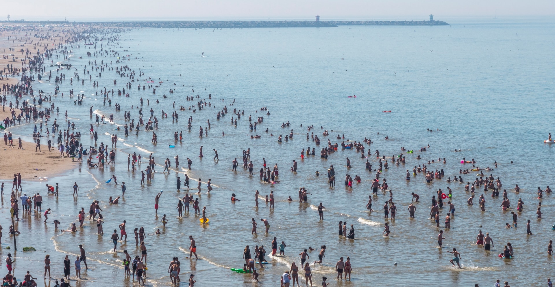 Mensen zoeken verkoeling in zee aan het strand bij Scheveningen.